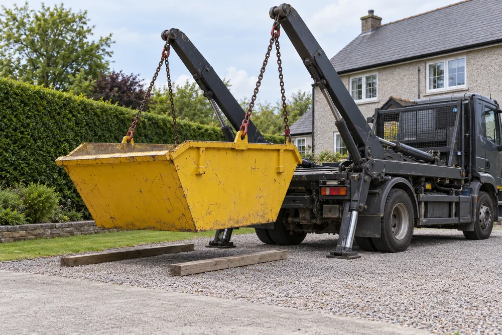 Unbranded skip lorry delivering a yellow skip to a clear driveway